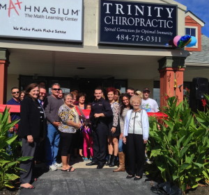 Dr. Joey Gaglioti (front, holding scissors) celebrates the Trinity Chiropractic ribbon-cutting with clients, guests, family and friends.